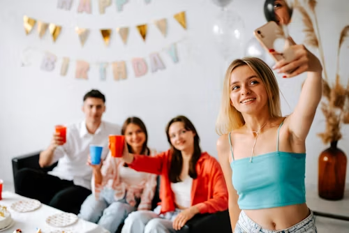 A woman taking a selfie at a party, representing shared experiences and digital projections.